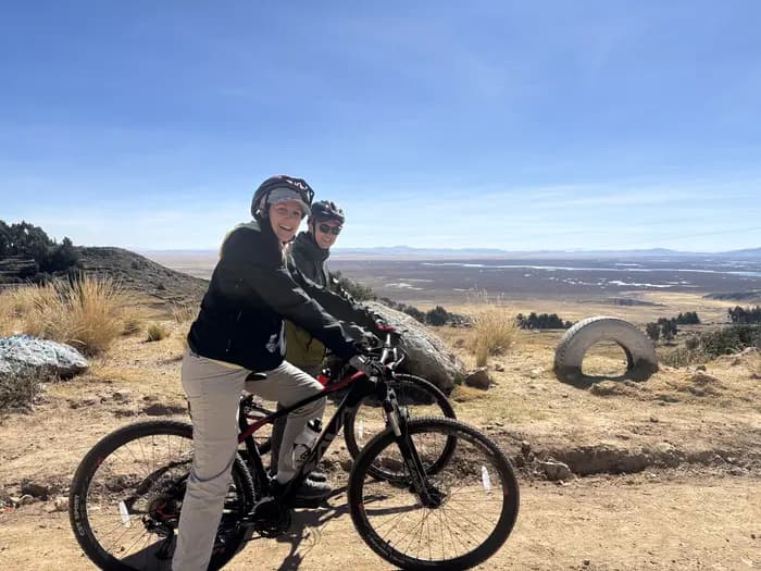 Cyclist standing on a rock above Lake Titicaca with their bike beside them