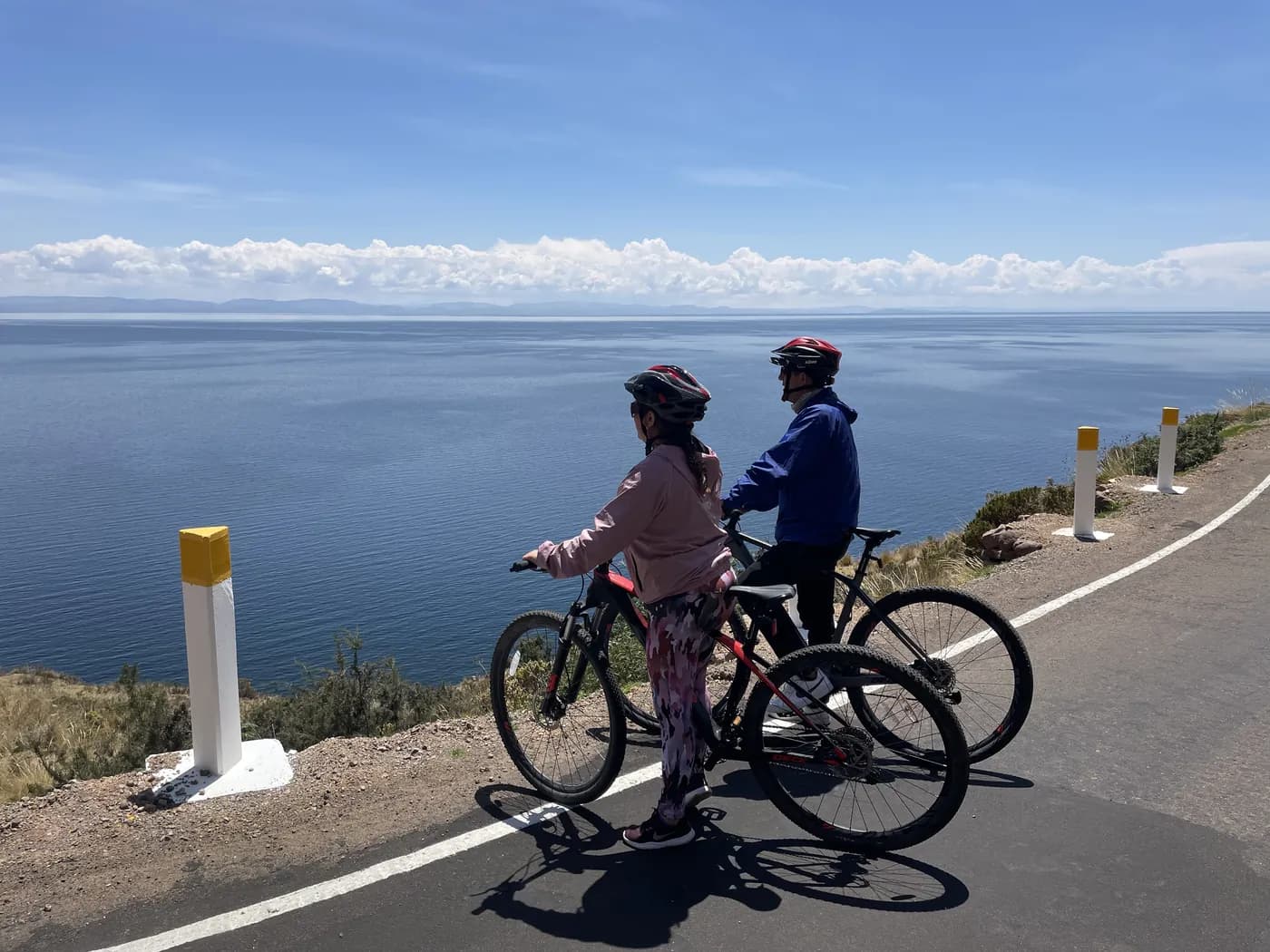 Cyclist standing on a rock above Lake Titicaca with their bike beside them