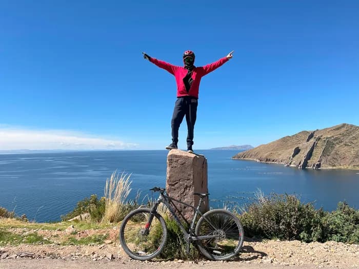 Cyclist standing on a rock above Lake Titicaca with their bike beside them