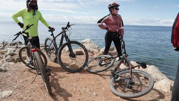Cyclist standing on a rock above Lake Titicaca with their bike beside them