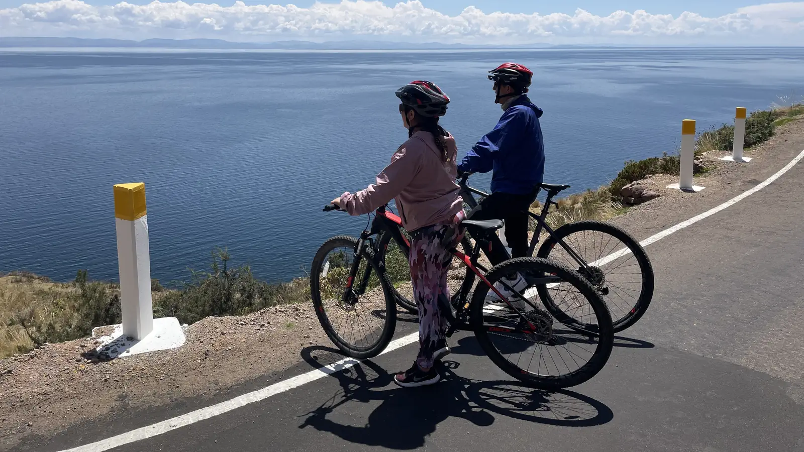 Two cyclists on the shoreline road with Lake Titicaca behind